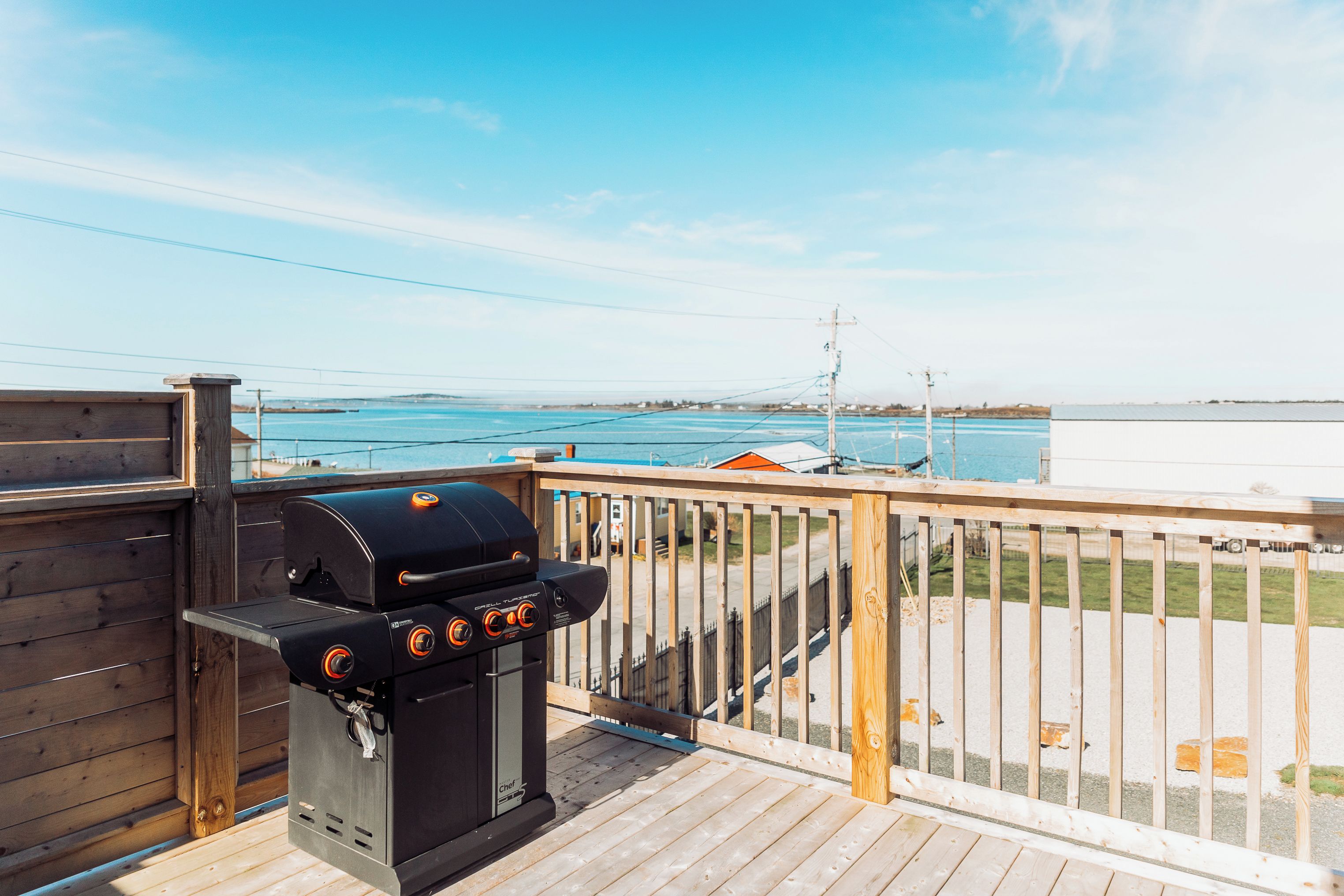 Un barbecue installé sur une terrasse en bois, offrant une vue sur une étendue d’eau et sur la terre ferme au loin.