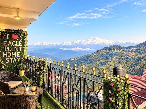Ein Balkon mit Korbmöbeln, einem Blumentopf und Blick auf schneebedeckte Berge.