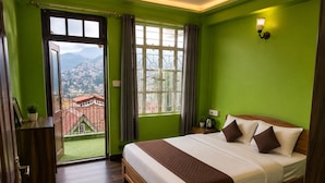 Een hotelkamer met een groot bed, uitzicht op de stad door het raam, en een balkon met uitzicht op de bergen.