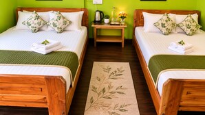 Een hotelkamer met twee houten bedden, groene wanden en een klein tafeltje met een waterkoker en bloemen.
