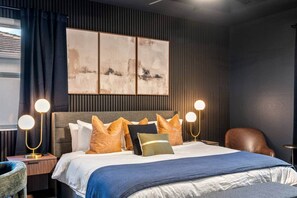 A modern hotel room with a bed, a headboard, a nightstand, a chair, and a wall-mounted artwork. - Saltwater Pool -12Hole Miniature Golf & Pickleball (South Miami Heights)