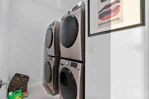 A laundry area with four stacked washing machines, a basket, and cleaning supplies. - Saltwater Pool -12Hole Miniature Golf & Pickleball (South Miami Heights)
