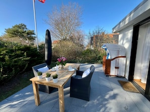 Eine Terrasse im Freien mit einem Holztisch und Stühlen, einem Blumentopf und einem Korbstuhl.
