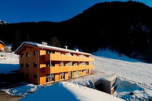 Ein mehrstöckiges Holzgebäude mit einer Skipiste im Hintergrund.