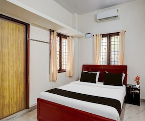 A hotel room with a bed, curtains, an air conditioning unit, a nightstand, and a window with a view. - Deluxe Ambience Home (Chennai)