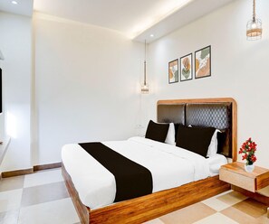 A modern hotel room with a large bed, wooden headboard, and a bedside table with a vase of flowers. - Deluxe Ambience Home (Chennai)