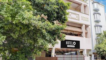 A hotel with a sign indicating it is company-serviced, a gated entrance, and a large tree in the foreground.
