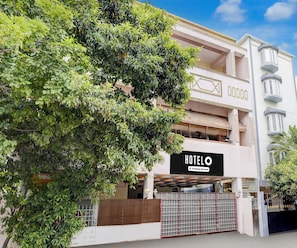 A hotel with a sign indicating it is company-serviced, a gated entrance, and a large tree in the foreground. - Deluxe Ambience Home (Chennai)