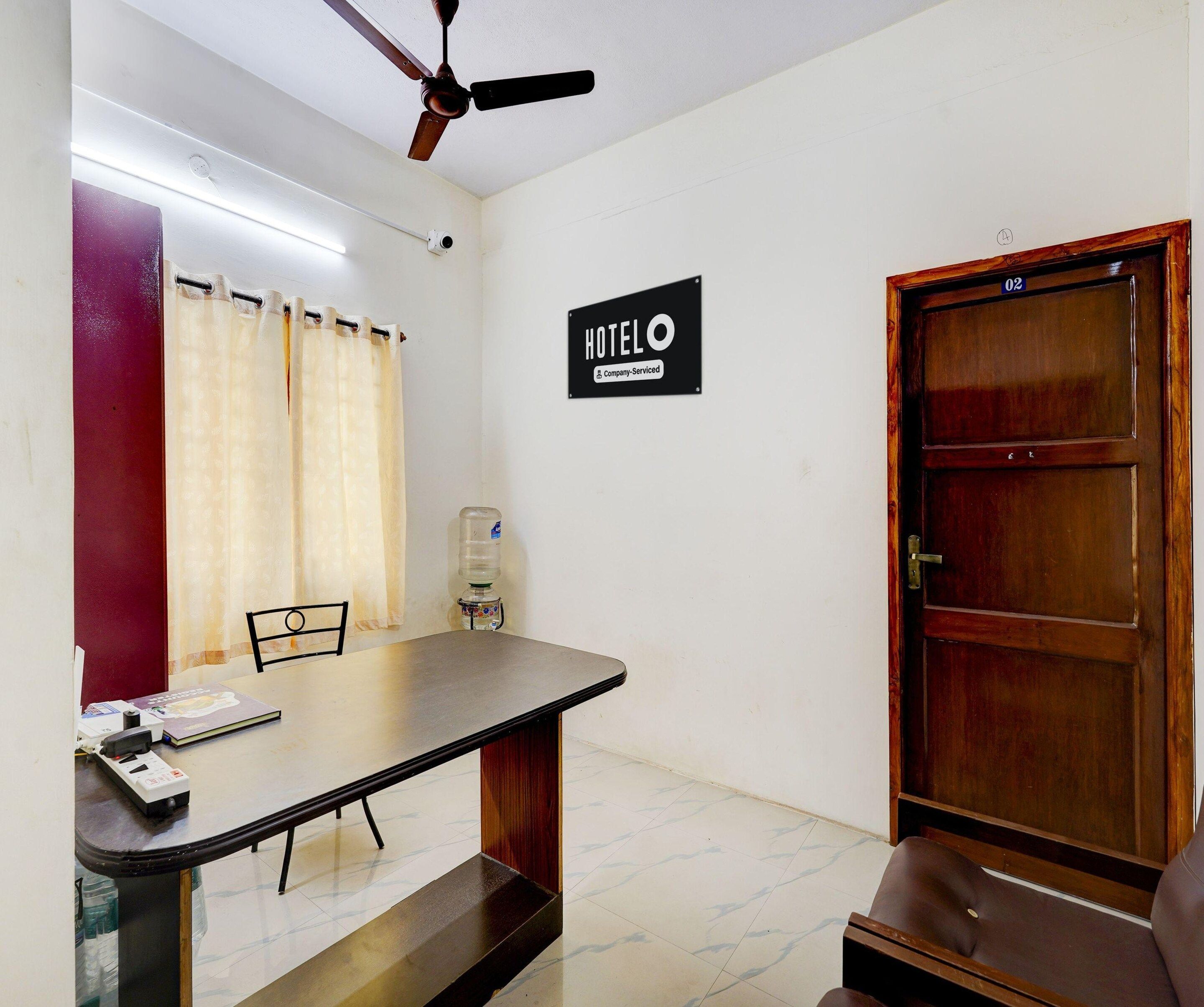 A hotel room with a bed, a desk, a chair, a water dispenser, a ceiling fan, and a door.
