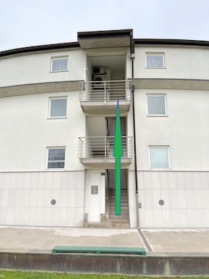 Ein mehrstöckiges Gebäude mit flachem Dach, einem Balkon im oberen Stockwerk und einer Treppe zum Eingang.