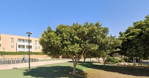 A building with a flat roof, a paved area, and a tree in the foreground. - Apartment With Pool and Golf Course Views in Roquetas de Mar (Roquetas de Mar)