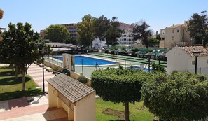 A swimming pool with a tiled deck, surrounded by greenery and buildings in the background. - Apartment With Pool and Golf Course Views in Roquetas de Mar (Roquetas de Mar)