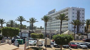 A hotel with multiple floors, a parking lot with cars, and palm trees. - Apartment With Pool and Golf Course Views in Roquetas de Mar (Roquetas de Mar)