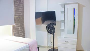 Un dormitorio con una cama, un televisor montado en la pared, un ventilador de pie y un armario.