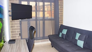 A room with a television mounted on a brick wall, a sofa with cushions, and a window with a view of buildings. - 41 September Promo in The Coolest Neighborhood (Medellín)