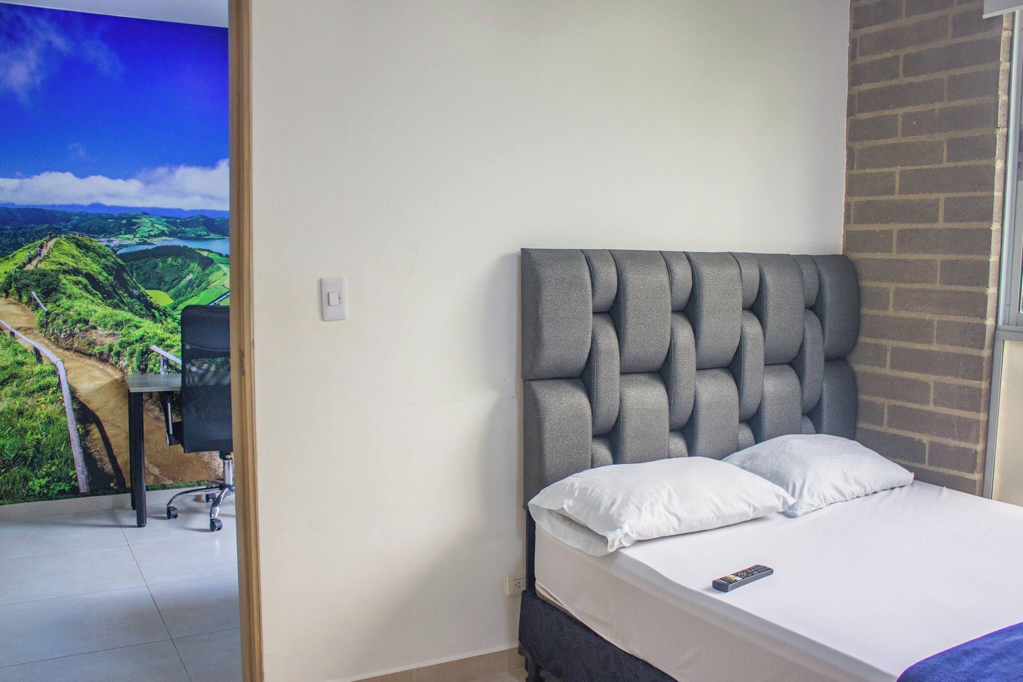 A bedroom with a bed, a desk, and a view of a landscape through an open door.