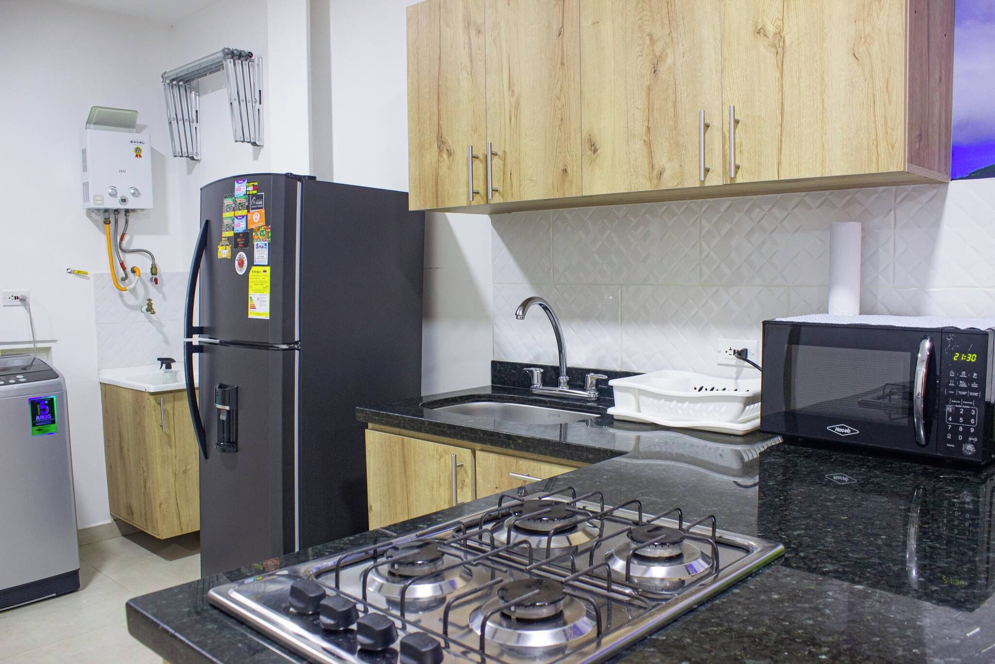 Cocina compacta con estufa a gas, microondas, refrigerador y alacenas de madera.