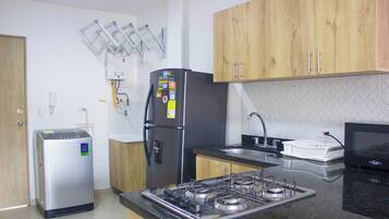 Cocina compacta con refrigerador, estufa, lavamanos y armarios de madera.