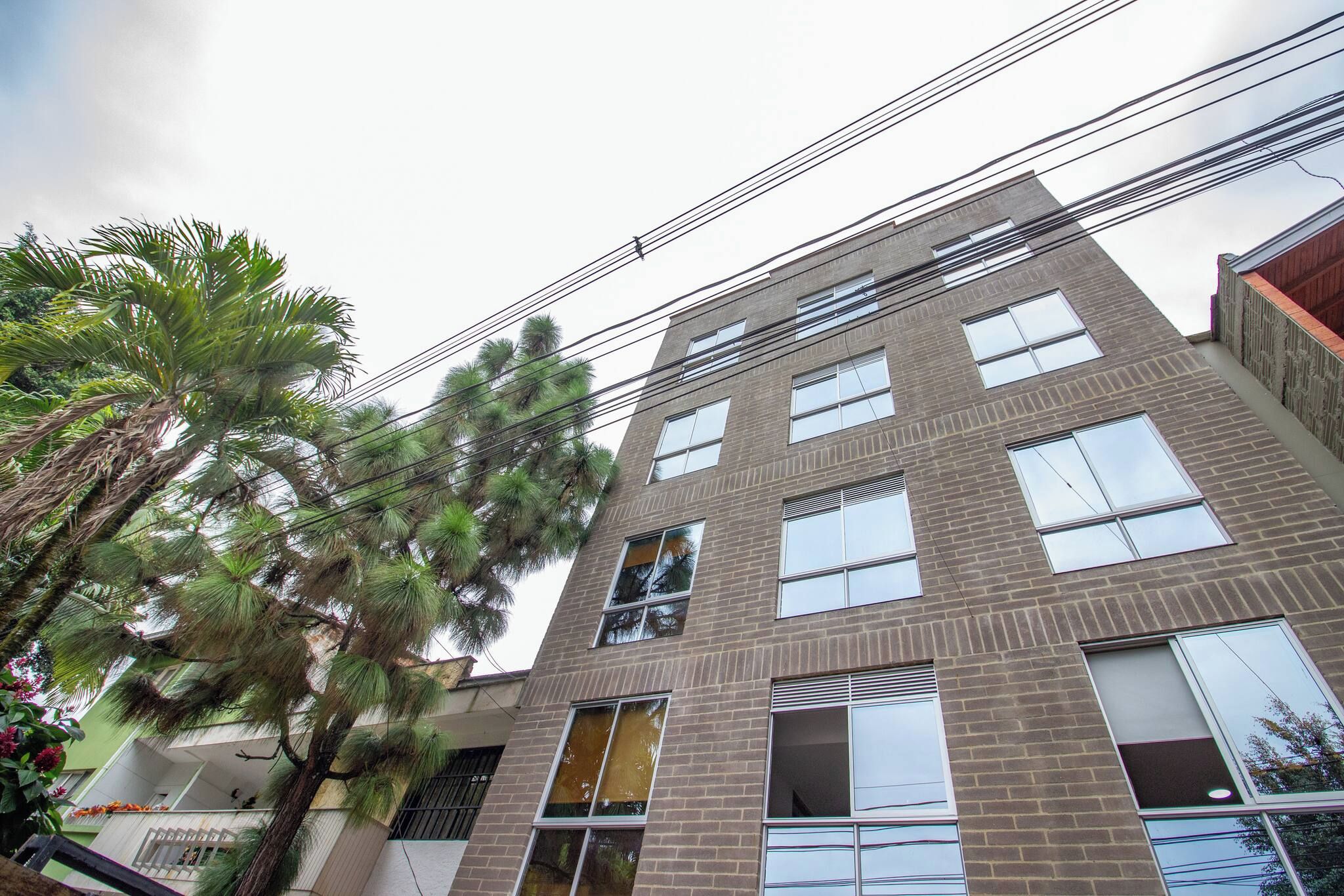 Un edificio de varios pisos con fachada de ladrillo, ventanas grandes y un balcón visible en el segundo piso.
