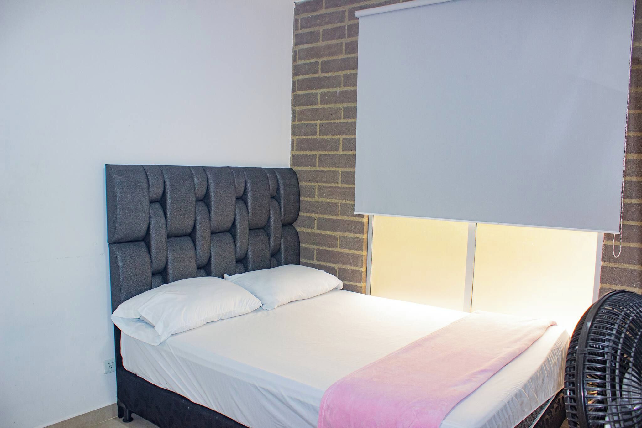 Una cama con cabecera, una ventana con persiana y una silla.