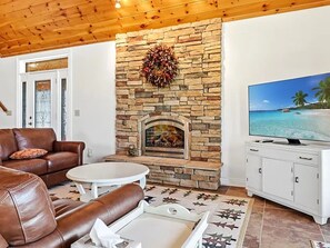 Ein Wohnzimmer mit Kamin aus Stein, Ledersofa, weißem Fernsehschrank und einem Strandbild am Fernseher.