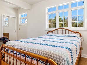Ein Schlafzimmer mit einem großen Bett, einem Holzkopfteil und einem Fenster mit Blick auf Bäume.