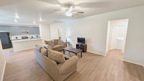 A modern living room with a sofa, coffee table, and TV, connected to a kitchen area with appliances. - Modern Midland Retreat (Midland)