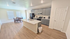 A kitchen with a central island, a dining area with chairs, and a trash can. - Modern Midland Retreat (Midland)