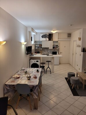 Een compacte keuken met witte kastjes, een eettafel met stoelen, en een klein barretje.