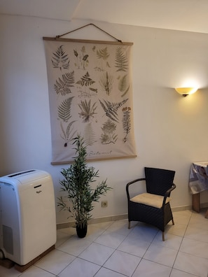 Ein Zimmer mit einem an der Wand befestigten Pflanzenmotiv, einem Standheizgerät, einer Topfpflanze und einem Stuhl.