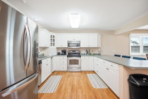 A modern kitchen with white cabinets, stainless steel appliances, and a wooden floor. - Asleep At The Reel: Waterway Home with Dock (Oak Island)