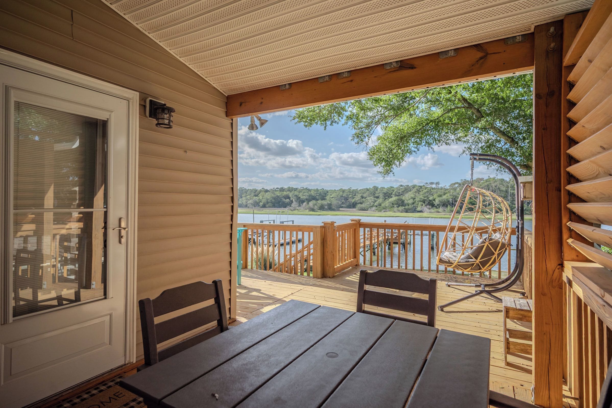 Une terrasse en bois avec une table et des chaises, une balançoire, et une vue sur un lac et une forêt.