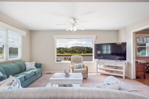 A living room with a sofa, a chair, a coffee table, a TV, and a view of a deck and trees. - Asleep At The Reel: Waterway Home with Dock (Oak Island)