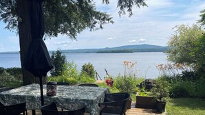 Un área de comedor al aire libre con una mesa, sillas, una terraza de madera y vistas a un lago.