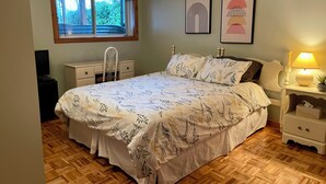Un dormitorio con cama, cómoda, silla, lámpara y dos cuadros en la pared.