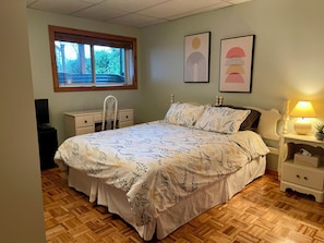 Ein Schlafzimmer mit einem Bett, einem Schminktisch, einem Sessel, einer Lampe und zwei gerahmten Bildern an der Wand.