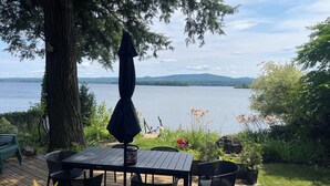 Una terraza de madera con una mesa y sillas, con vistas a un lago y montañas al fondo.