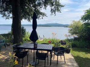 Eine Holzterrasse mit Tisch und Stühlen, mit Blick auf einen See und Berge in der Ferne.