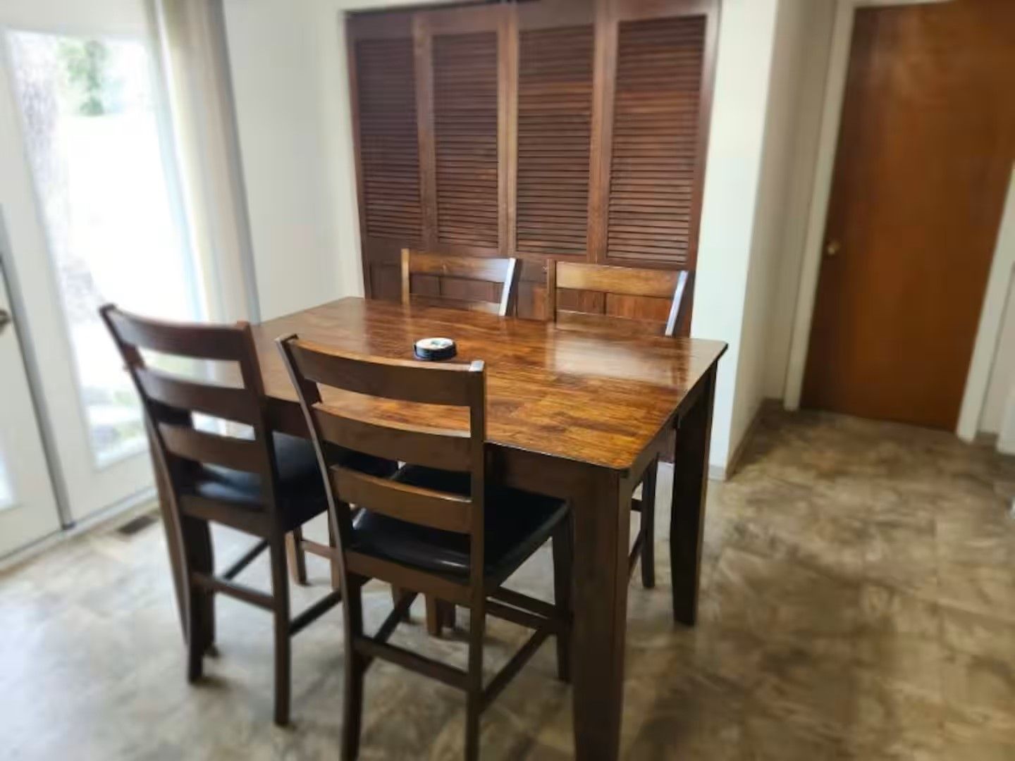 Une table à manger avec six chaises, une fenêtre avec des stores et une porte.