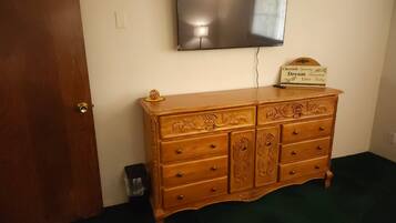 Une pièce avec une commode en bois, un téléviseur à écran plat fixé au mur et un panneau posé sur la commode.