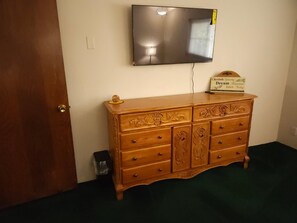 Une pièce avec une commode en bois, un téléviseur à écran plat fixé au mur et un panneau posé sur la commode.