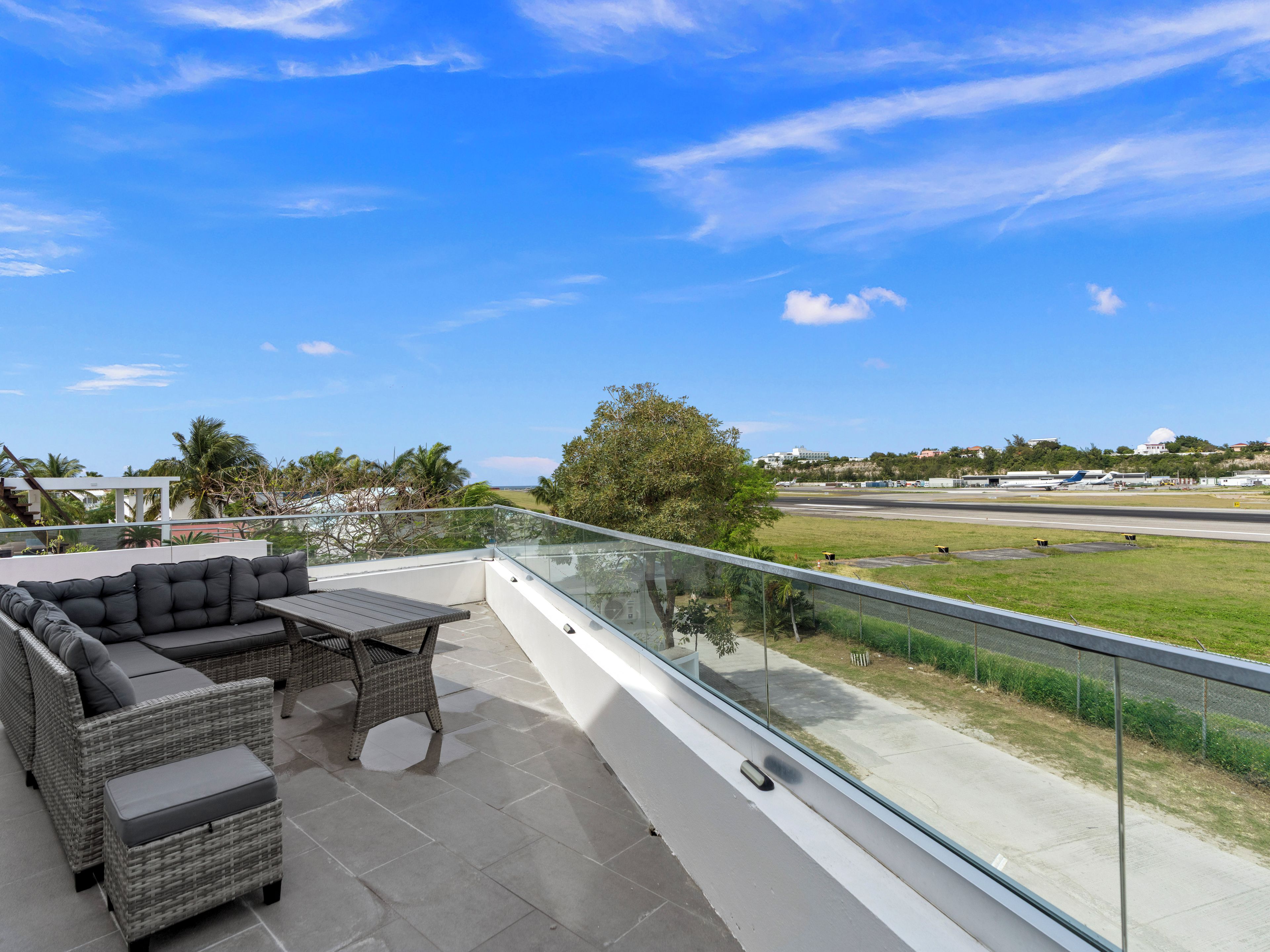 A balcony with outdoor furniture, a clear view of a runway, and a distant building.