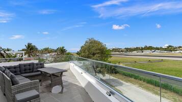 A balcony with outdoor furniture, a clear view of a runway, and a distant building.