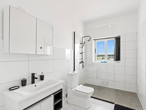 A modern bathroom with a white sink, mirror, and toilet, a shower with a window, and a tiled floor. - Luxurious 3-Bedroom Townhome 
@ White Sands Beachfront Villas
“Suite Serenity” (Simpson Bay)
