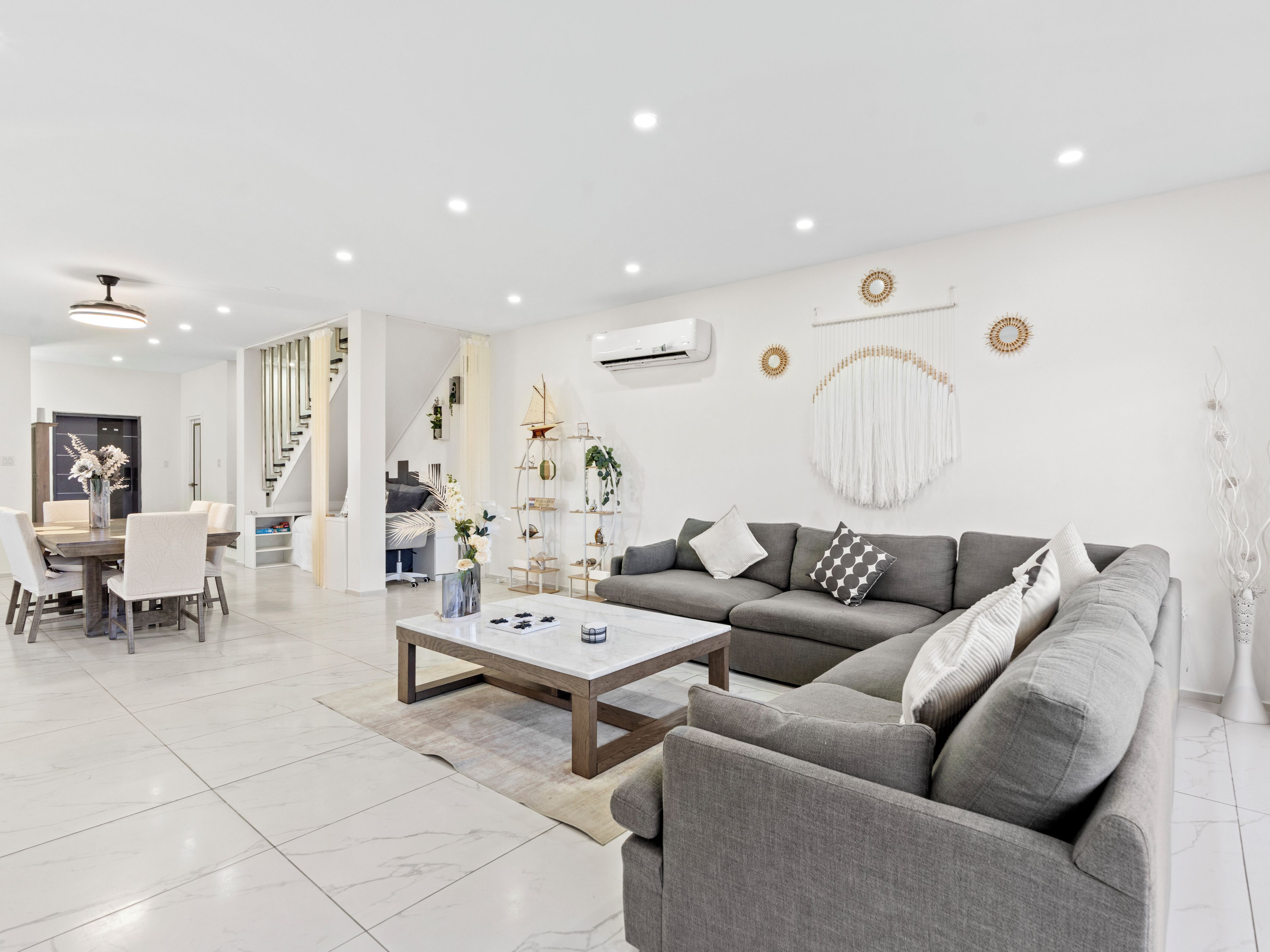 A modern living room with a grey sofa, a coffee table, and a dining area with chairs and a table.