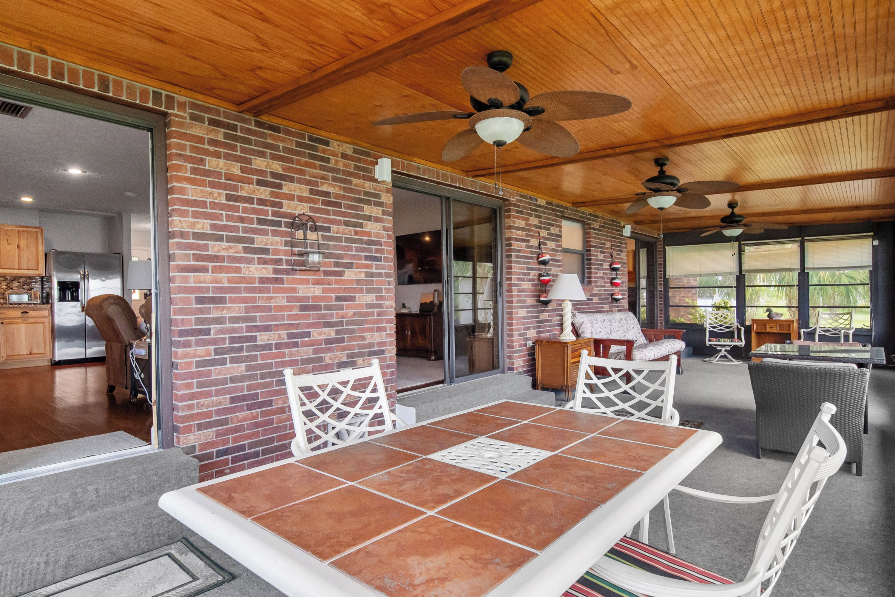 Un espacio de patio techado con pared de ladrillo, una mesa de comedor con sillas y ventiladores de techo.