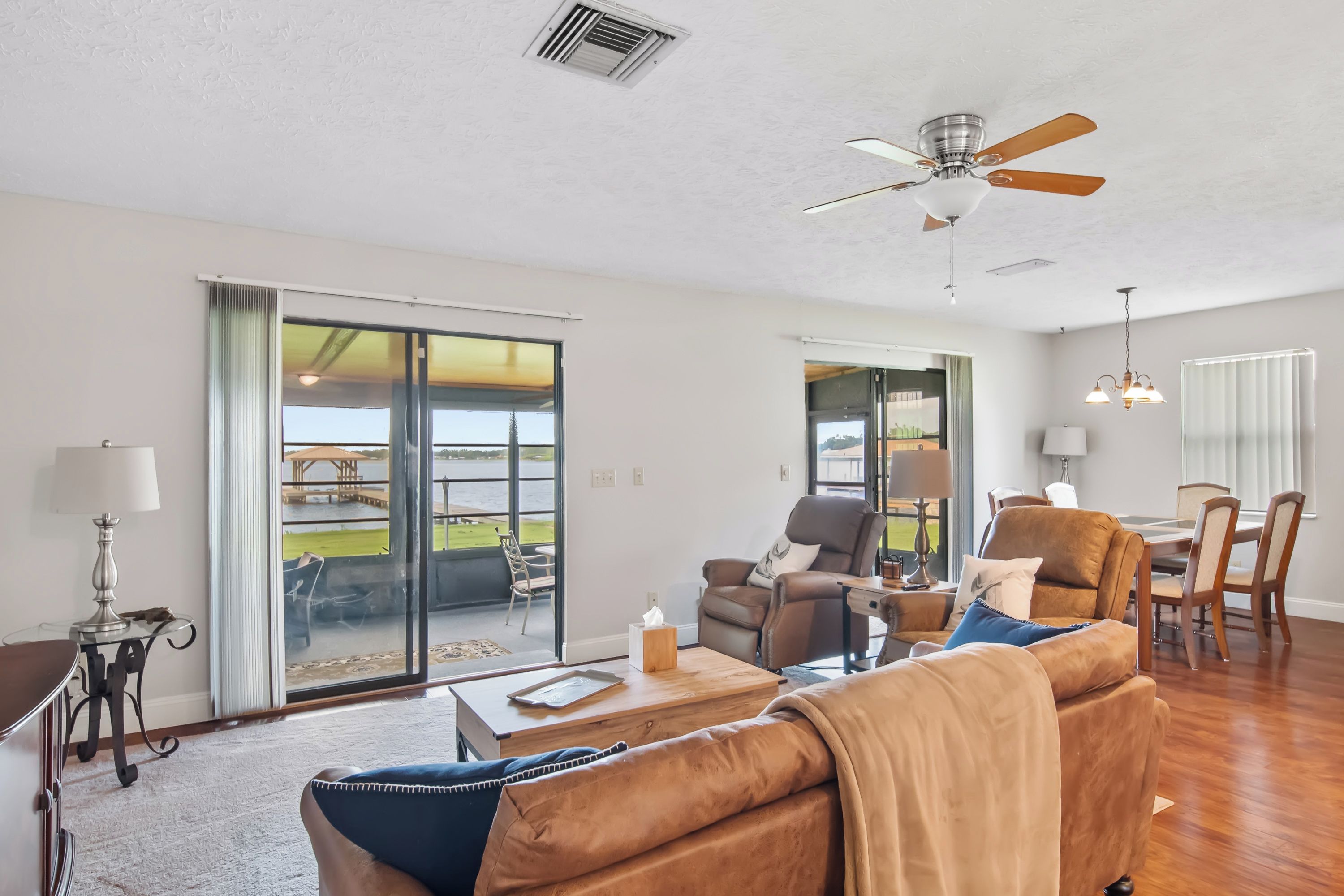 A spacious living room with a large sliding glass door leading to a balcony, a ceiling fan, and a dining area with a table and chairs.