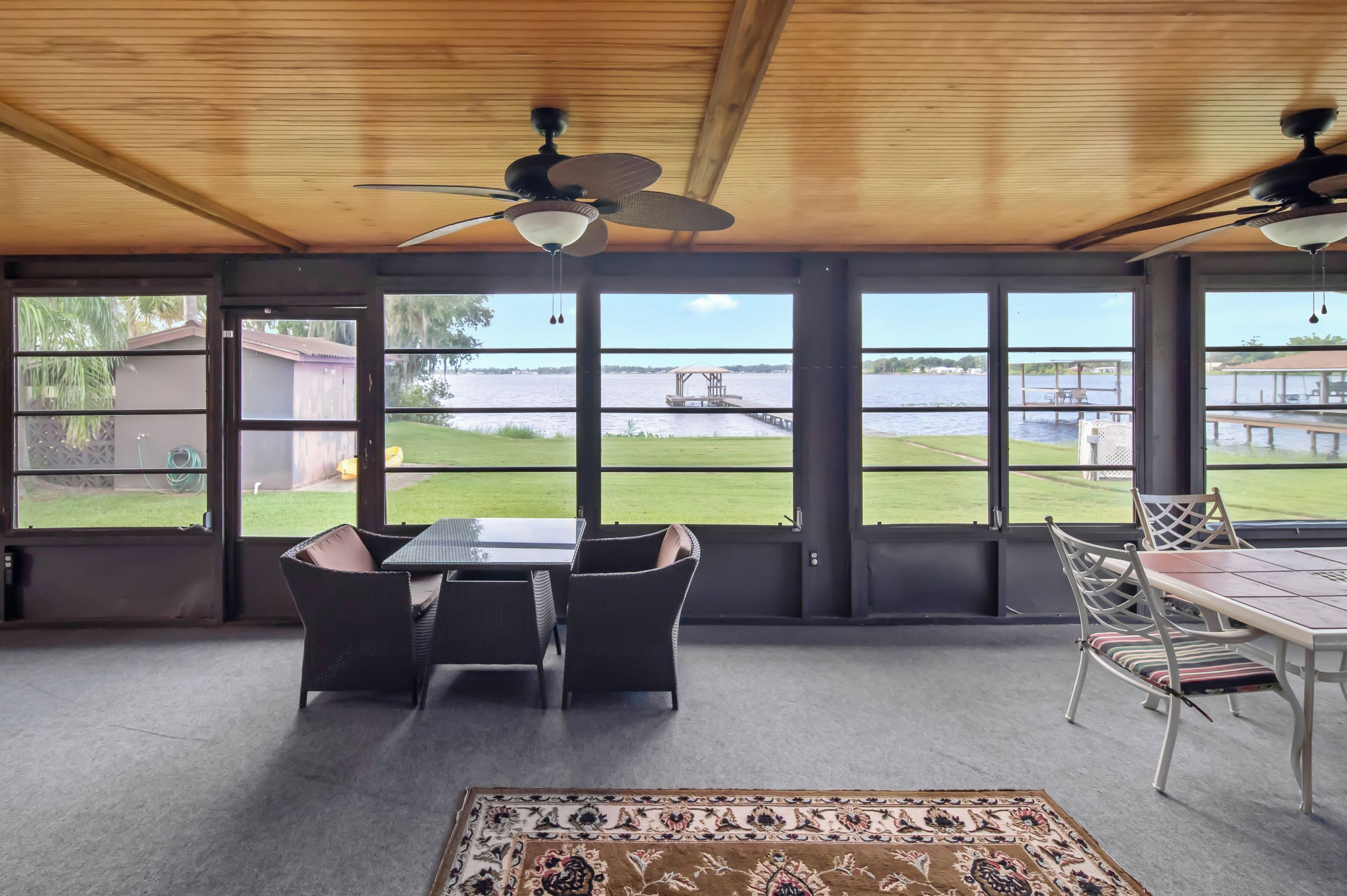 A spacious room with a large table and chairs, a ceiling fan, and a view of a body of water through large windows.