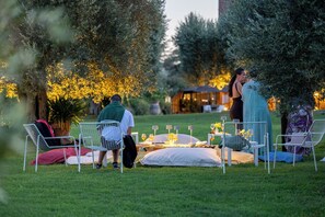 Un área de comedor al aire libre con sillas y mesas de metal, rodeada de follaje y árboles.