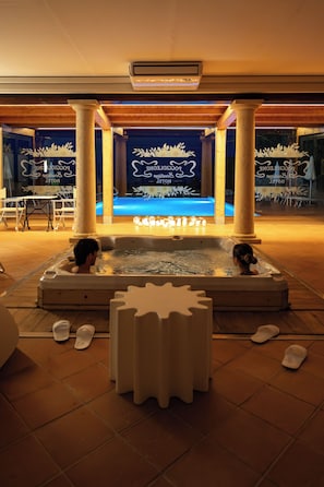 Un espace de bien-être avec un jacuzzi, des colonnes en bois et une piscine en arrière-plan.